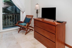 Un bureau en bois, un téléviseur à écran plat, une lampe et une chaise avec un coussin.