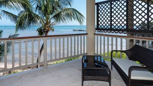 Een balkon met een rieten bank en een tafeltje, met uitzicht op een strand met een palmboom en een pier.