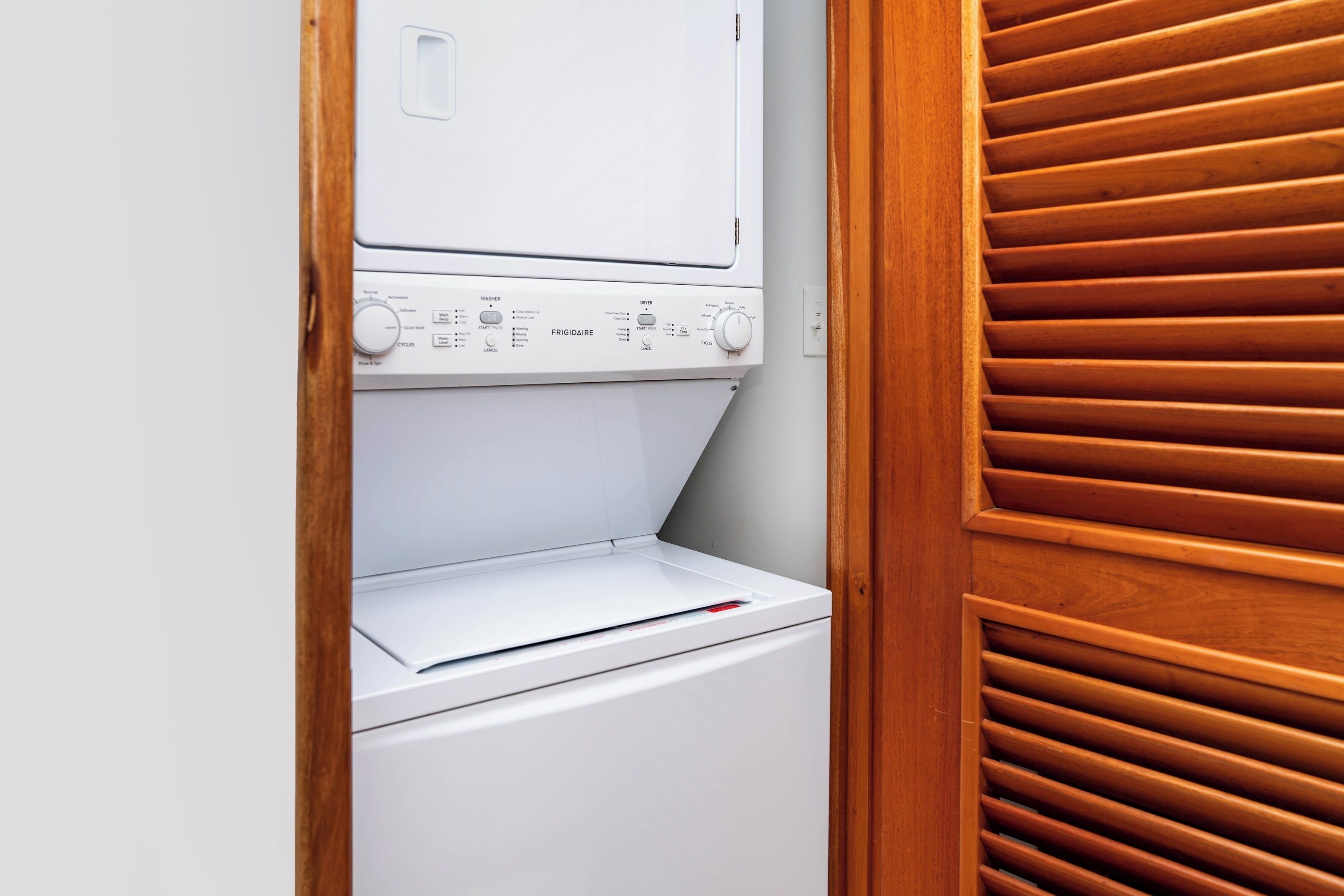 A white washing machine in a laundry room with wooden blinds.