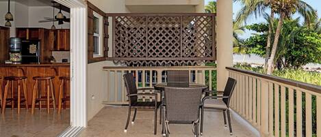 A balcony with a dining table and chairs, a kitchen area with bar stools, and a view of palm trees.
