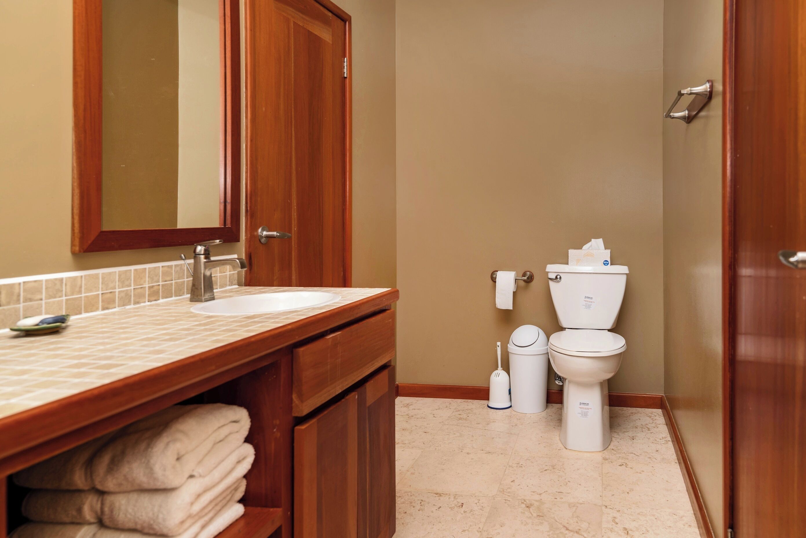 Une salle de bain avec un meuble-lavabo en bois, un évier, un miroir, des toilettes et une poubelle.