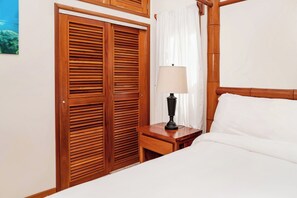 Un dormitorio con estructura de cama de madera, una mesita de noche con lámpara y un armario con puertas batientes.