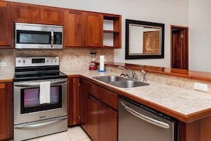 A modern kitchen with stainless steel appliances, wooden cabinets, a double sink, and a built-in oven. - Tranquil Oasis: Stylish 1BR Condo in Ambergris Caye! (San Pedro Town)