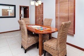 A dining area with a wooden table and wicker chairs, a woven partition, and a mirror on the wall. - Tranquil Oasis: Stylish 1BR Condo in Ambergris Caye! (San Pedro Town)