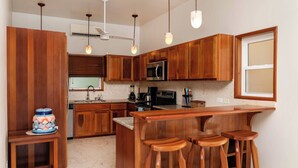 Een keuken met houten kastjes, een magnetron, een spoelbak en een bar met krukjes.