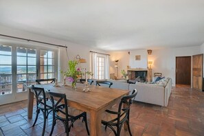 Uma sala de estar espaçosa com uma mesa de jantar de madeira, cadeiras pretas, um sofá e uma lareira.