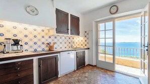 A kitchen with a tiled backsplash, wooden cabinets, a dishwasher, and a view of the sea through a glass door.