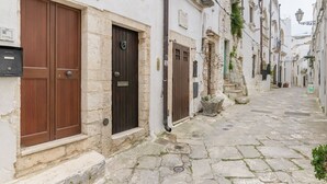 Uma rua estreita de paraleipípedos com edifícios de pedra tradicionais, portas de madeira e um pequeno degrau de entrada.