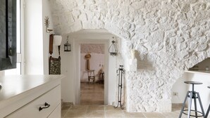 Um quarto com parede de pedra, porta de madeira, uma mesa pequena e um banquinho.