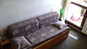 A wooden sofa with patterned cushions in a room with a plain wall and a window. - Ski-in/ski-out & foot of the slopes, 2nd floor, balcony, tv, ski locker, 19m², Samoëns (Samoëns)