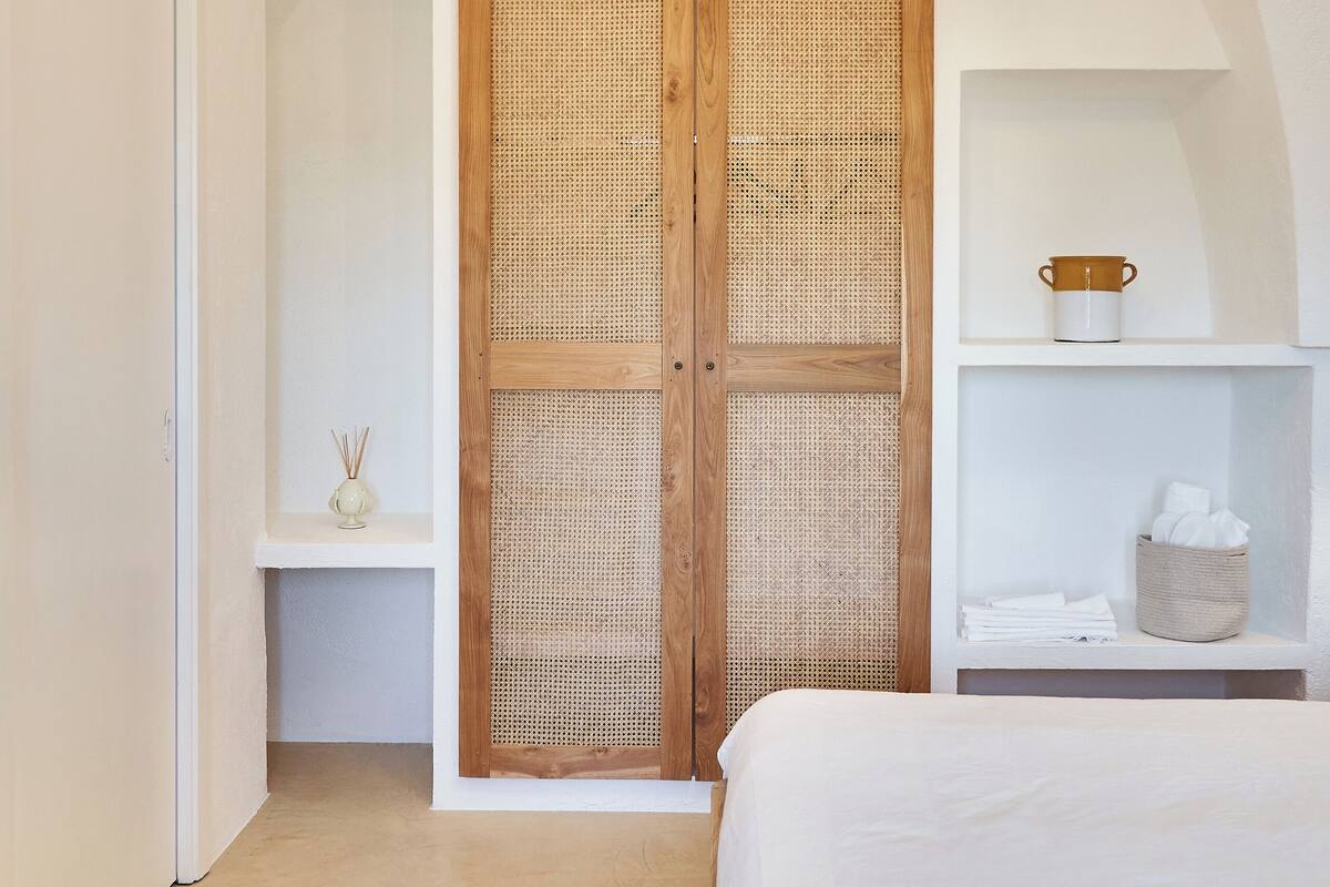 Un dormitorio con una cama grande, un armario de madera, una repisa con una taza y una lámpara colgante.