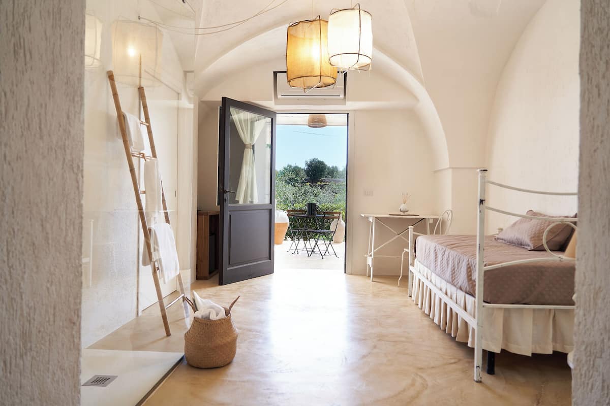 Un dormitorio con cama, una mesita, una lámpara y vistas al exterior.