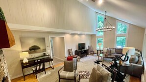 A spacious living room with a high ceiling, a television, a fireplace, and a large window providing natural light. - Spacious home <1 min from Lincoln Peak! Fits the whole extended family (Warren)