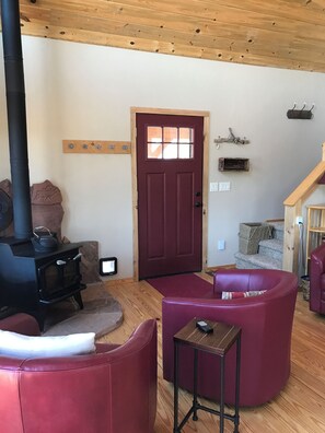 A cozy living room with a wood-burning stove, red leather sofas, and a wooden ceiling.
