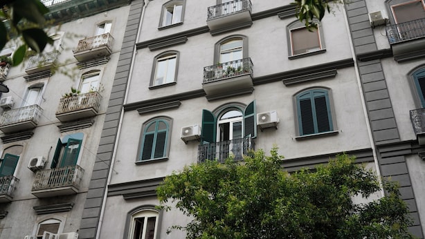 Un immeuble à plusieurs étages doté de balcons, de climatiseurs et de volets verts.