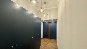 Un couloir avec des casiers bleu foncé, un plancher en bois et des luminaires suspendus aux formes géométriques.