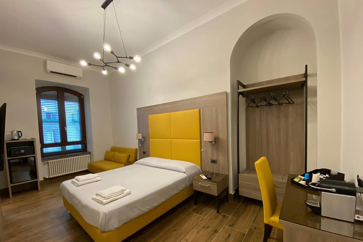 A modern hotel room with a large bed, a desk, a chair, and a wardrobe.