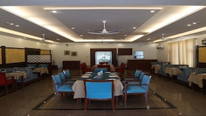 A restaurant with a central dining table surrounded by blue chairs, booths on the sides, and ceiling fans. - Flamingo Tourist Resort (Hisar)