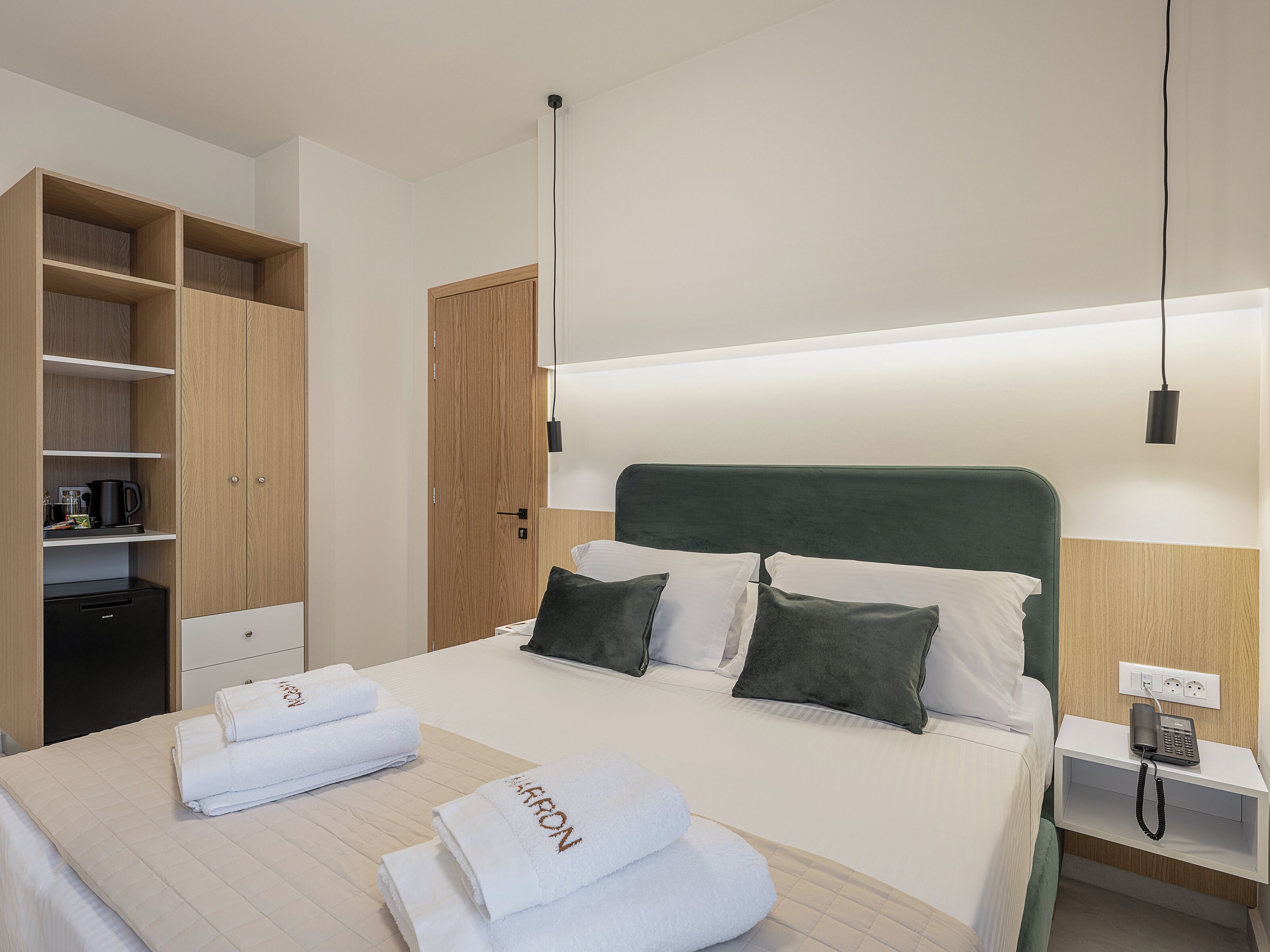 Une chambre d’hôtel comprenant un lit, une table de chevet avec un téléphone, une commode, une armoire et une étagère avec des articles de toilette.