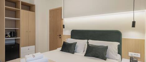 Une chambre d’hôtel comprenant un lit, une table de chevet avec un téléphone, une commode, une armoire et une étagère avec des articles de toilette.