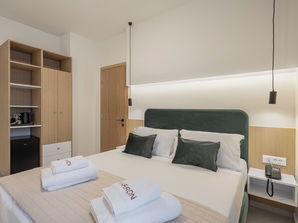 A hotel room with a bed, a bedside table with a phone, a nightstand, a wardrobe, and a shelf with toiletries. - Miss Marrone City Hotel (Chania)
