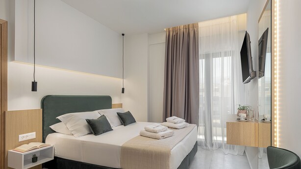 Una habitación de hotel moderna con una cama grande, mesitas de noche, un televisor y un espejo con luces.