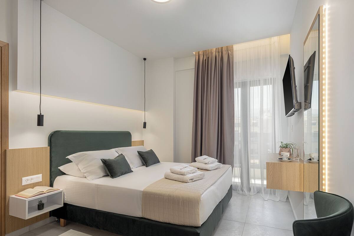 Ein modernes Hotelzimmer mit einem großen Bett, Nachttischen, einem Fernseher und einem beleuchteten Spiegel.