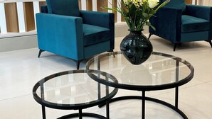 Un interior moderno con dos sillones azul verdoso, una mesa de centro de cristal y un separador de madera con plantas.