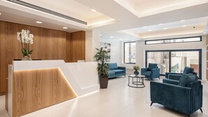 Un área de recepción moderna con mostrador de madera, sofás azules y un amplio ventanal con vistas a la ciudad.