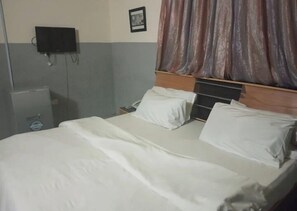 A hotel room with a bed, a bedside table, a TV mounted on the wall, and a curtain. - Beeland Hotel Abuja (Abuja)