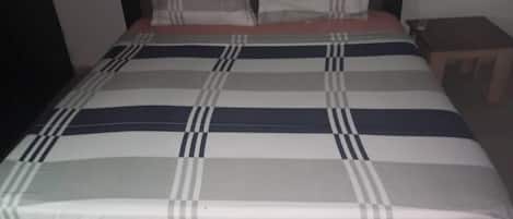 A bed with a striped bedspread, a pillow, and a nightstand with a lamp.
