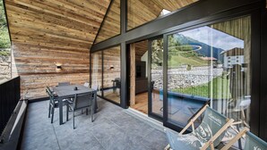 A modern outdoor dining area with a wooden ceiling, a glass wall, and a view of a mountainous landscape. - sGmiatli – Hideaway Apartments (Kappl)