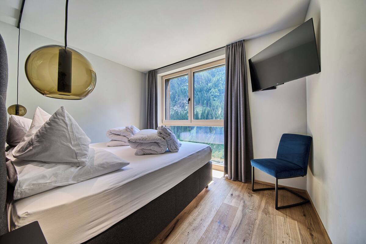 Un dormitorio moderno con una cama grande, un televisor de pantalla plana montado en la pared y vistas al exterior a través de una ventana.