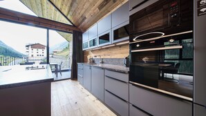 A modern kitchen with a wooden ceiling, built-in appliances, and a view of the mountains. - sGmiatli – Hideaway Apartments (Kappl)
