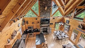 Un chalet confortable avec une cheminée en pierre, des murs en bois, une cuisine avec un coin bar et de grandes fenêtres.