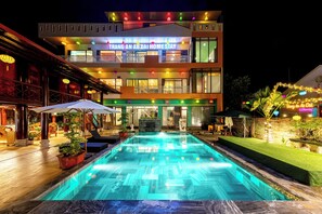 A modern hotel with a swimming pool, outdoor seating, and a well-lit facade. - Room in Chalet - Trang An Ao Dai Homestay - Wooden House With Field View and Private Bathroom (Ninh Binh)