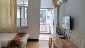 Hotellihuone, jossa on sänky, työpöytä, televisio ja parveke.