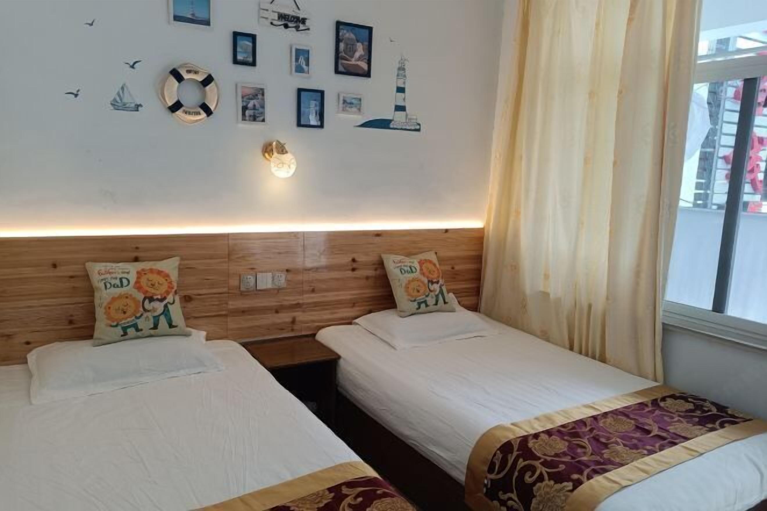 A hotel room with two beds, a wooden headboard, a wall with nautical-themed decorations, and a window with curtains.