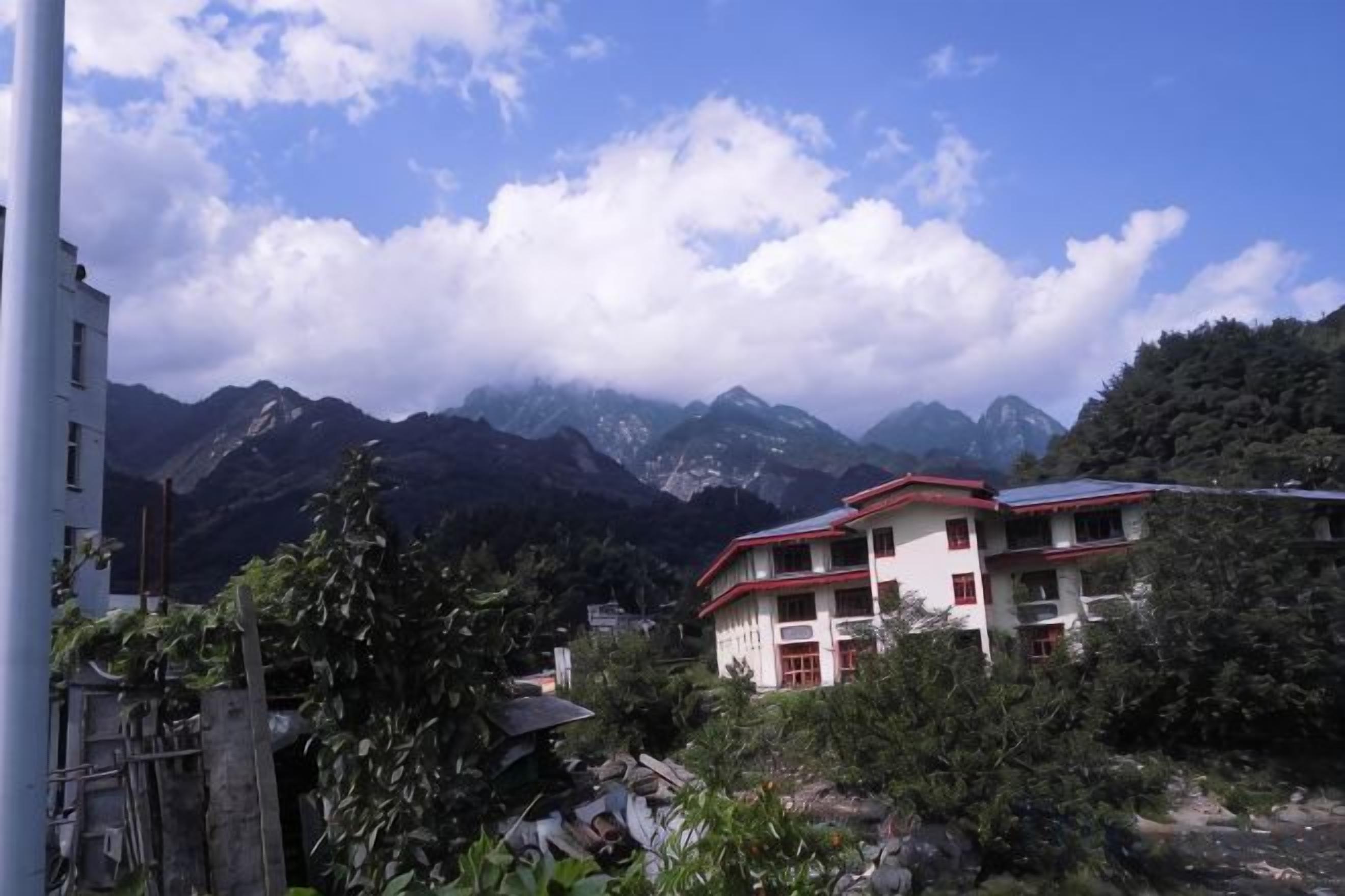 A building with multiple floors and a red roof, surrounded by greenery and mountains in the background.