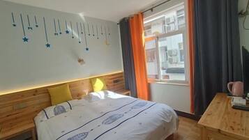 Un dormitorio con cama, cabecero de madera, ventana con cortinas, mesita de noche y una pared decorada con estrellas.