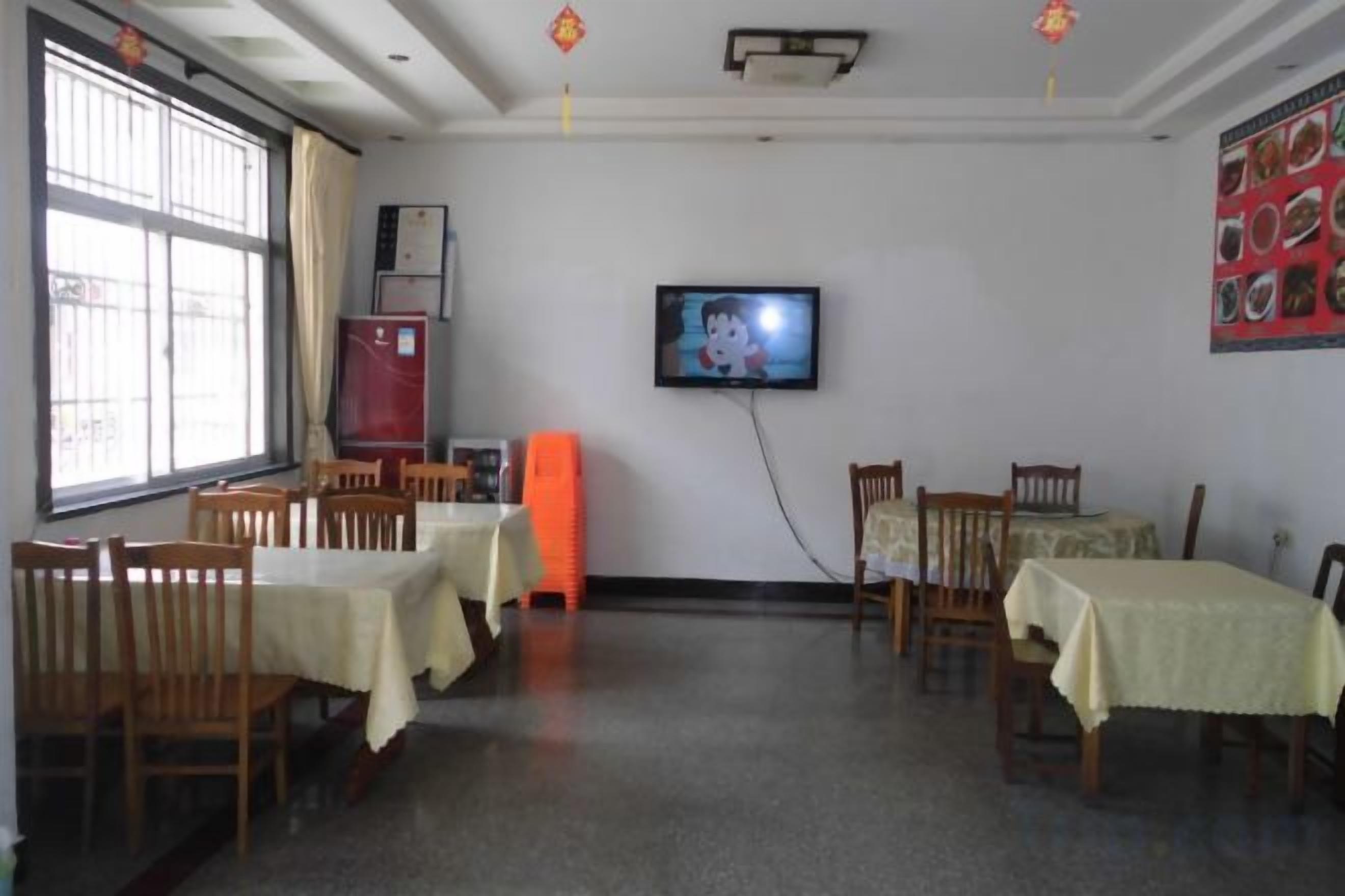 A dining area with tables and chairs, a television on the wall, and a window with curtains.