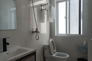 Ein Badezimmer mit Waschbecken, Toilette und Dusche. Ein Fenster sorgt für natürliches Licht.