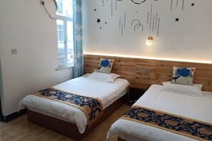 Ein Hotelzimmer mit zwei Betten, einem Holzkopfende, weißer Bettwäsche, Zierkissen, einem Nachttisch und einer Wand mit Sternen- und Konstellationsdekorationen.