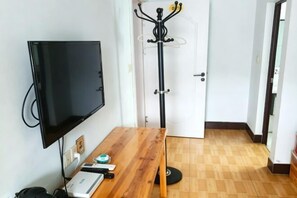 A room with a flat-screen TV mounted on the wall, a wooden table with a laptop, a coat rack, and a door leading to another room. - Mount Huangshan Jiayuan Inn (Huangshan City)