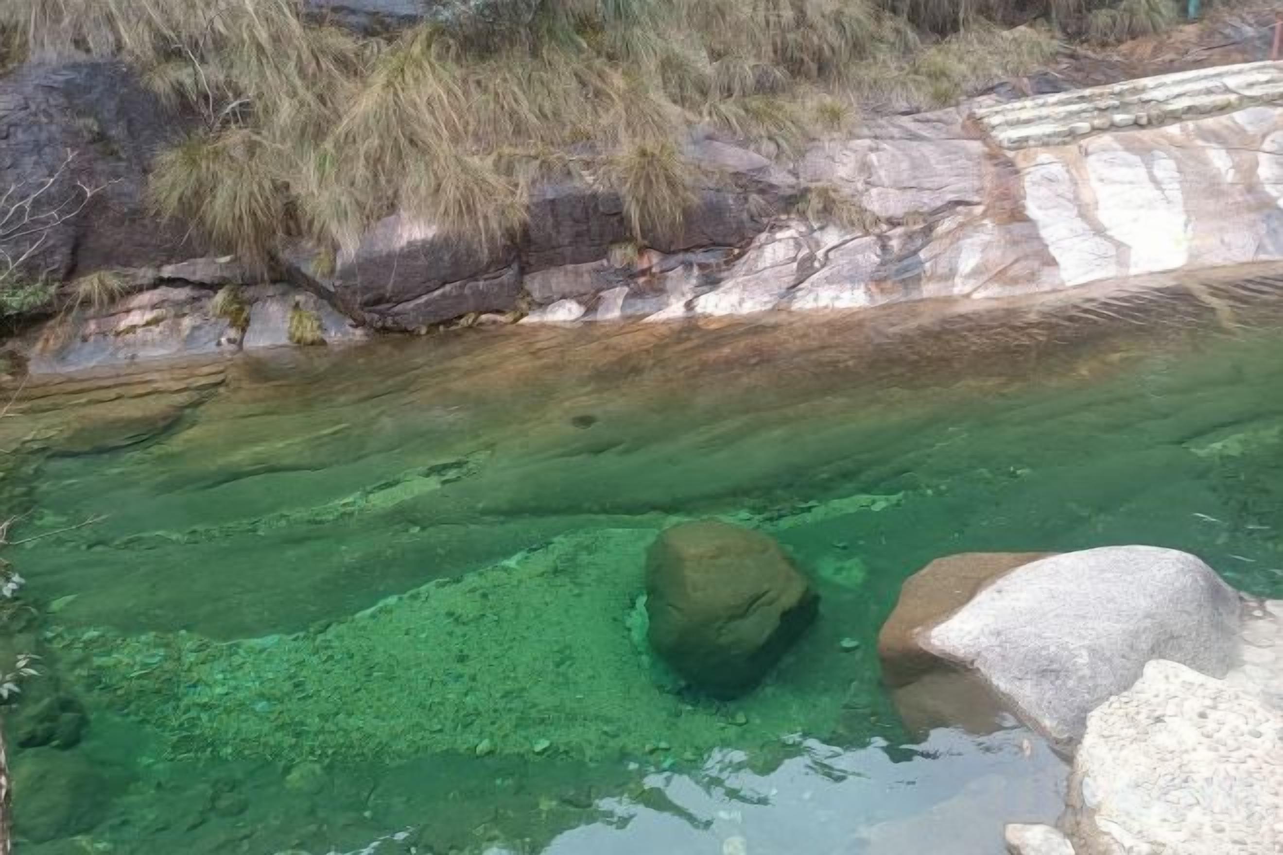 En naturlig pool med klart vatten, omgiven av stenar och växtlighet.