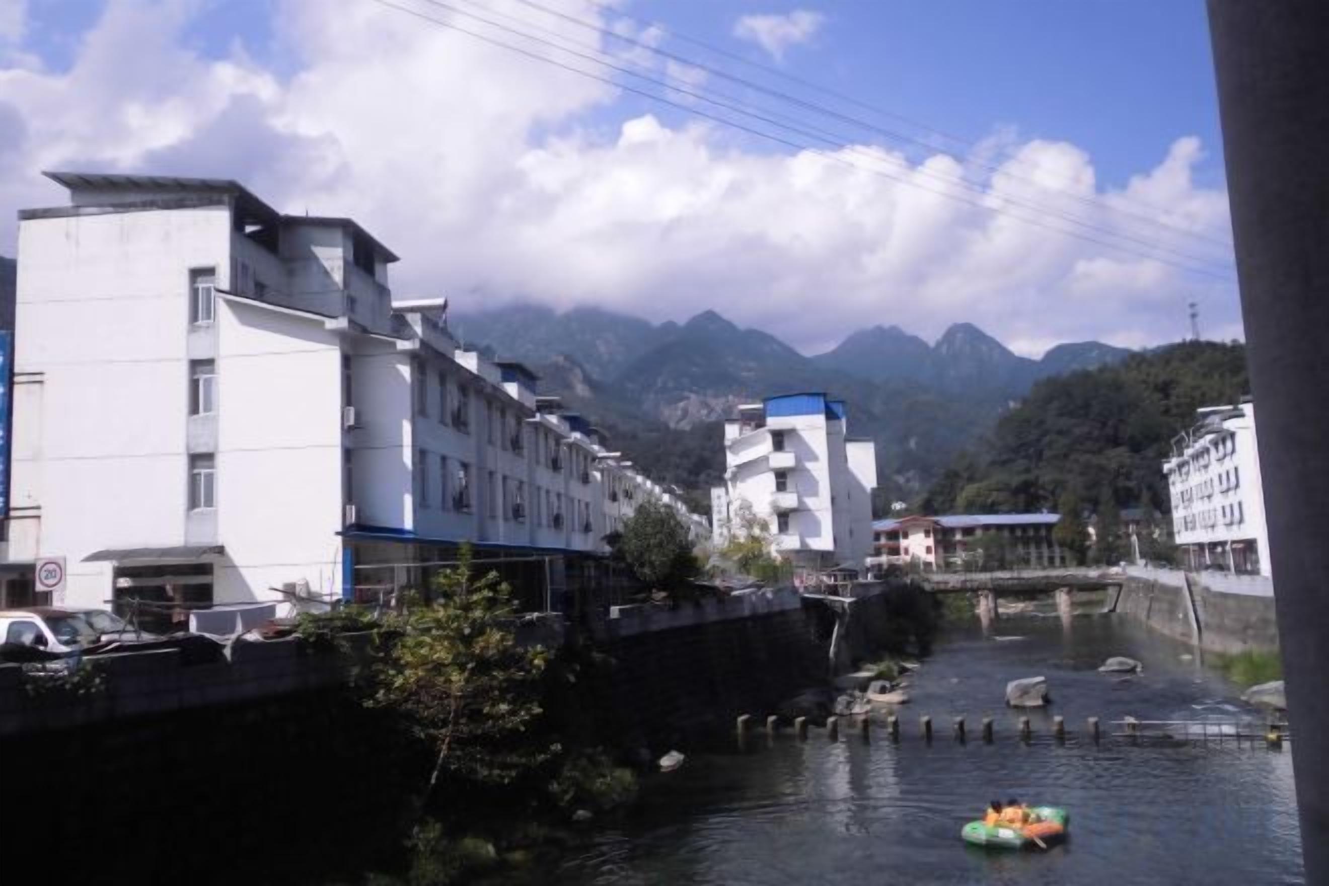 Um rio com um barco, edifícios ao longo da margem e montanhas ao fundo.