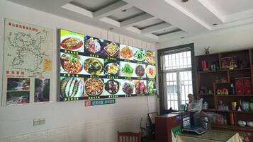 A dining area with a large wall display of various dishes, a map, and a bookshelf.