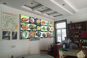Uma sala de jantar com um grande painel na parede exibindo diversos pratos, um mapa e uma estante de livros.