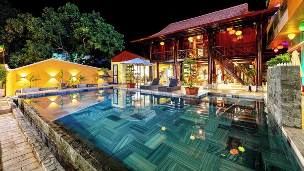 A swimming pool with a clear water surface, surrounded by a stone wall and a wooden deck. - Room in House - Trang An Ao Dai Homestay - Family Room With Field View and Private Bathroom (Ninh Binh)