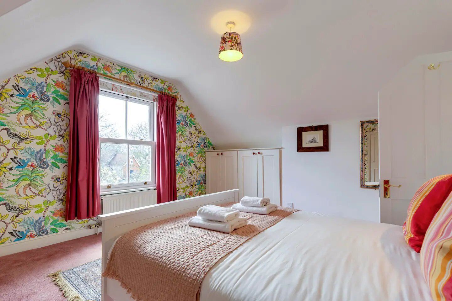 A bedroom with a bed, a window with curtains, a wardrobe, and a mirror on the wall.